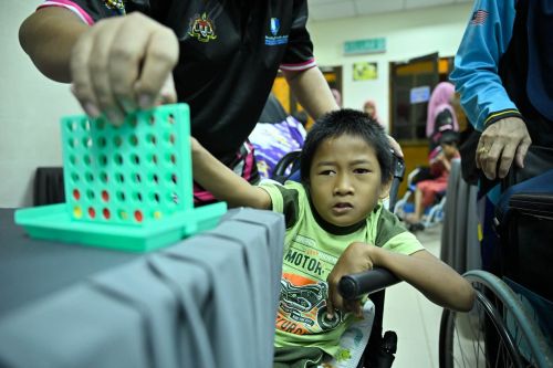 Langkah kecil, semangat besar. Seorang kanak-kanak mencuba permainan susun cakera dengan bimbingan petugas.
